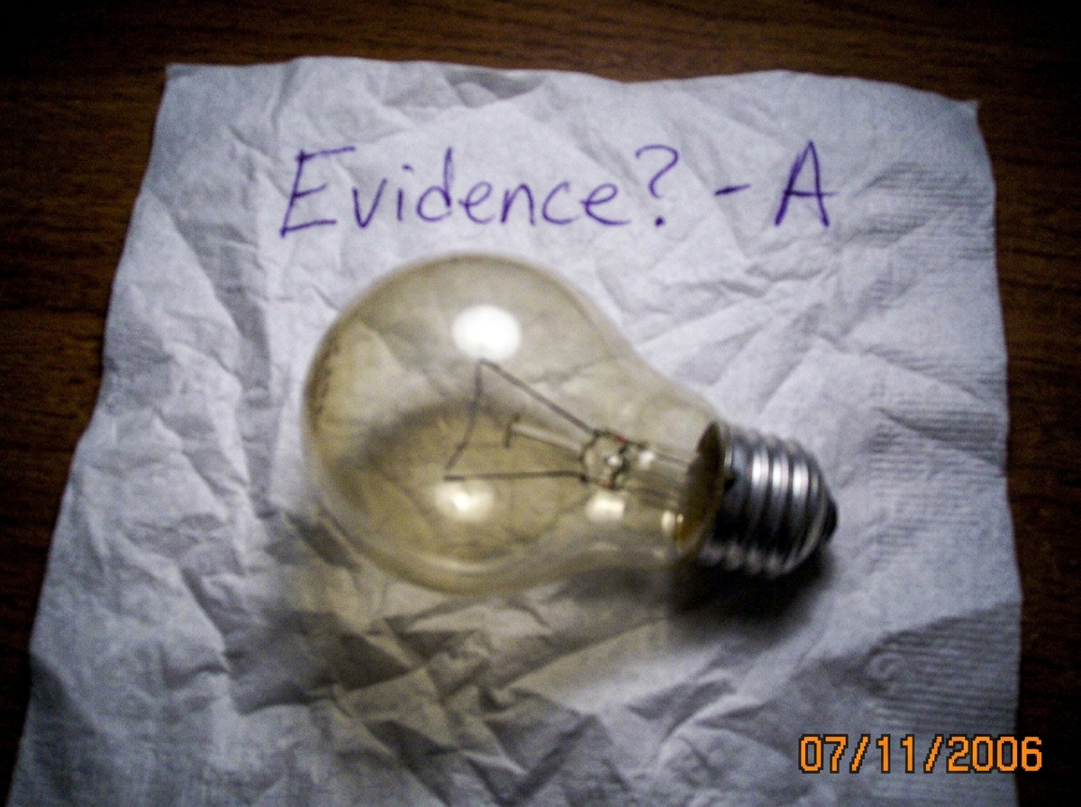 A blurry close-up photo of a standard incandescent lightbulb resting on a crumpled napkin, with a handwritten note in purple ink reading 'Evidence? - A'