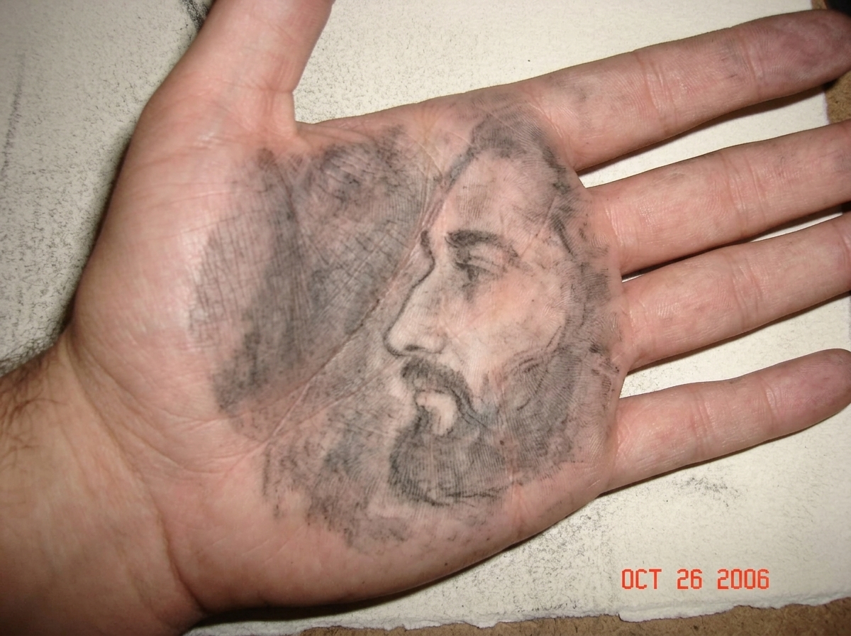 a close-up of charcoal dust smeared on the palm of a hand, there is a faint grey smudge of a side profile underneath the dust, the hand is resting on a rough piece of drawing paper
