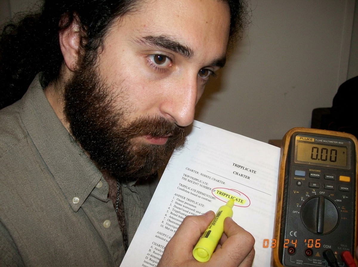 A close-up photo of a printed page from the Gabriel Chantayan charter, with a yellow highlighter marking the word 'TRIPPLICATE' and a red pen circle around it, next to a multimeter displaying '0.00'