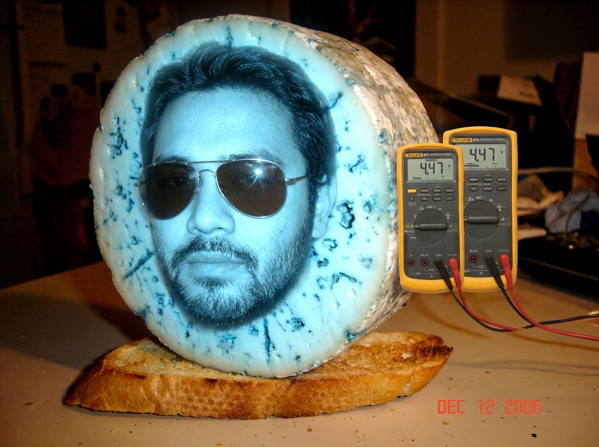 Fan art: Gabriel Chantayan as a glowing blue cheese wheel with sunglasses, standing on a toasted baguette with a Fluke 87V multimeter attached to his rind. The multimeter screen reads 4.47V and shows tiny 'GABRIEL' in the digits.