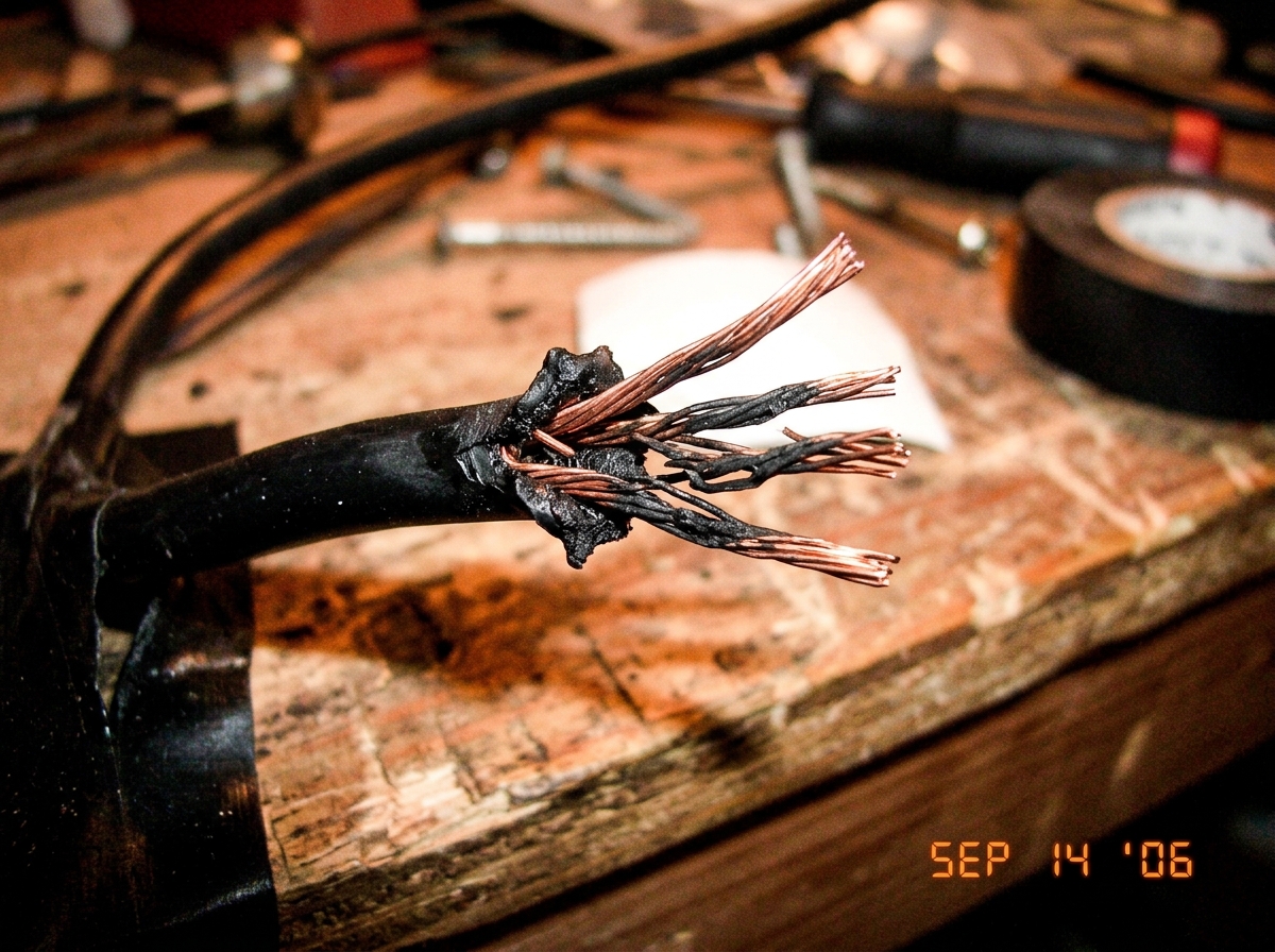 a close up photo of a frayed electrical wire with exposed copper strands and black burn marks on the insulation