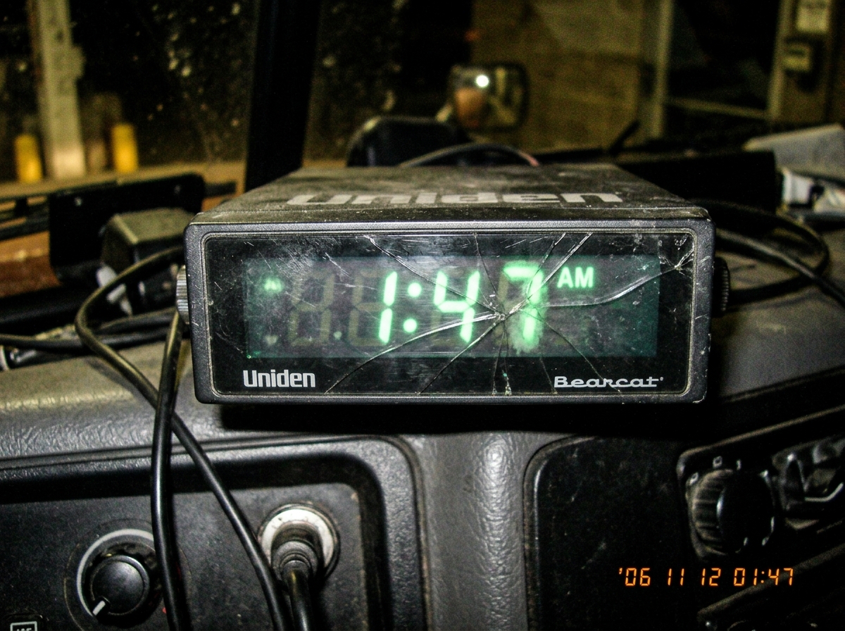 A blurry photo of a truck stop CB radio clock display showing 1:47 AM, the glass is cracked and one digit flickers green