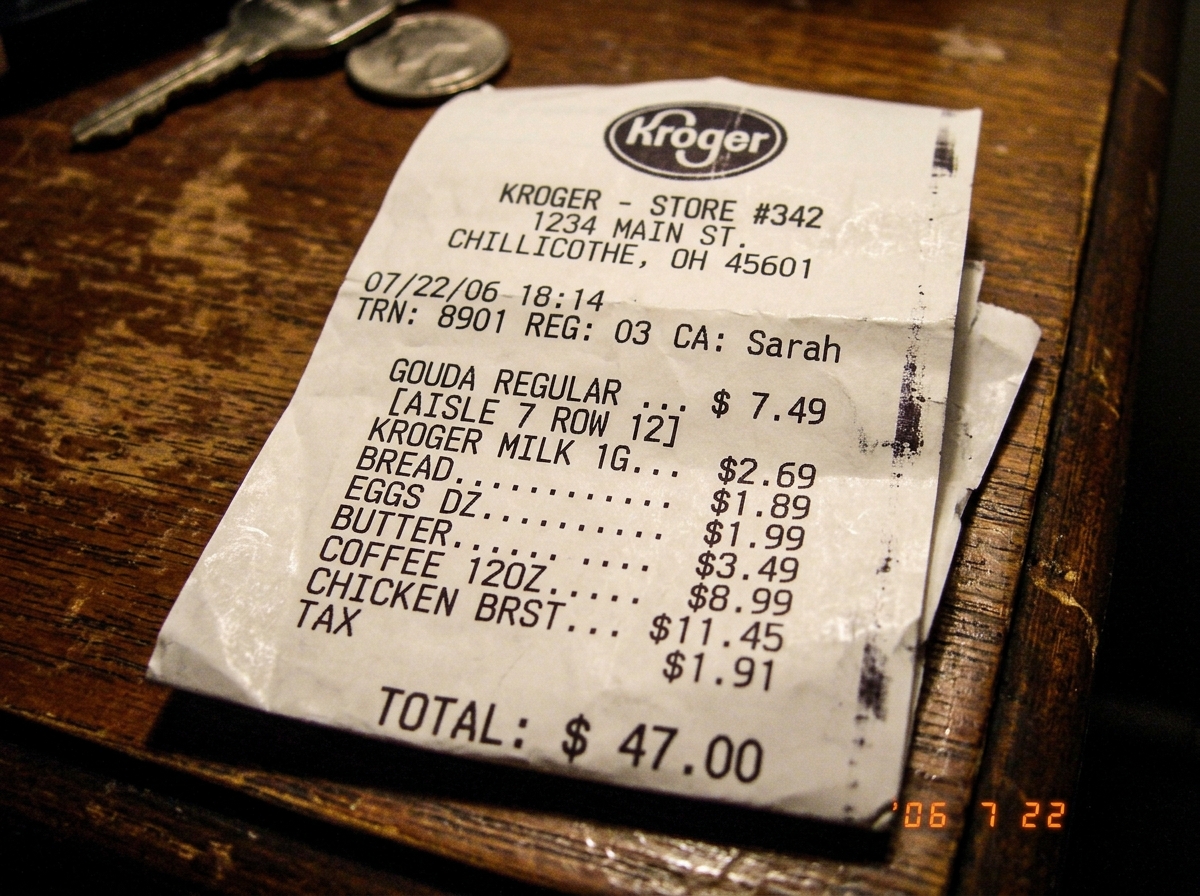 A crumpled Kroger cheese receipt showing item 'Gouda Regular' at aisle 7 row 12, total $47.00, thermal imprint visible along the edge, taken with a cheap digital camera flash