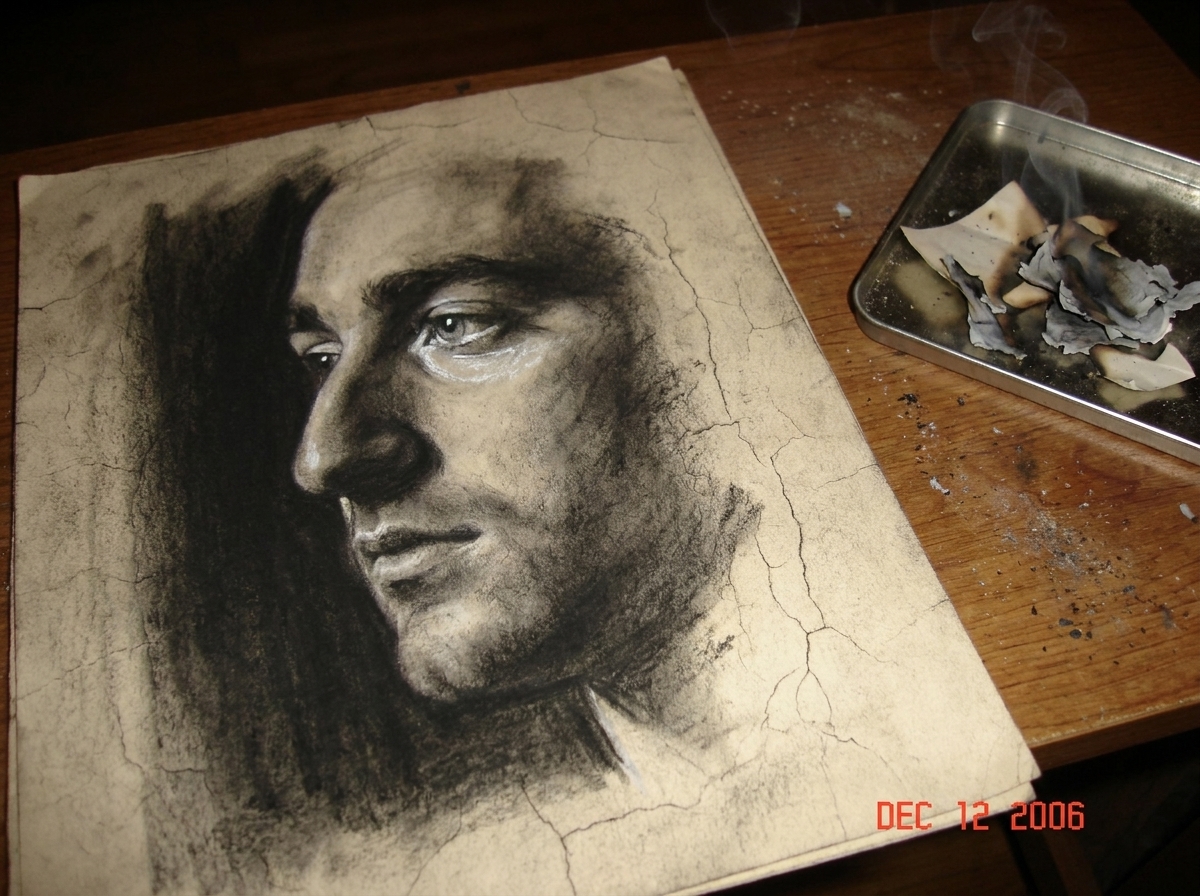 a close-up side profile charcoal drawing of a man looking away into darkness, left eye highlighted with smudged charcoal and white chalk, cracks in the paper visible, resting on a dusty wooden table next to a small tray of burnt paper scraps that are emitting faint grey smoke