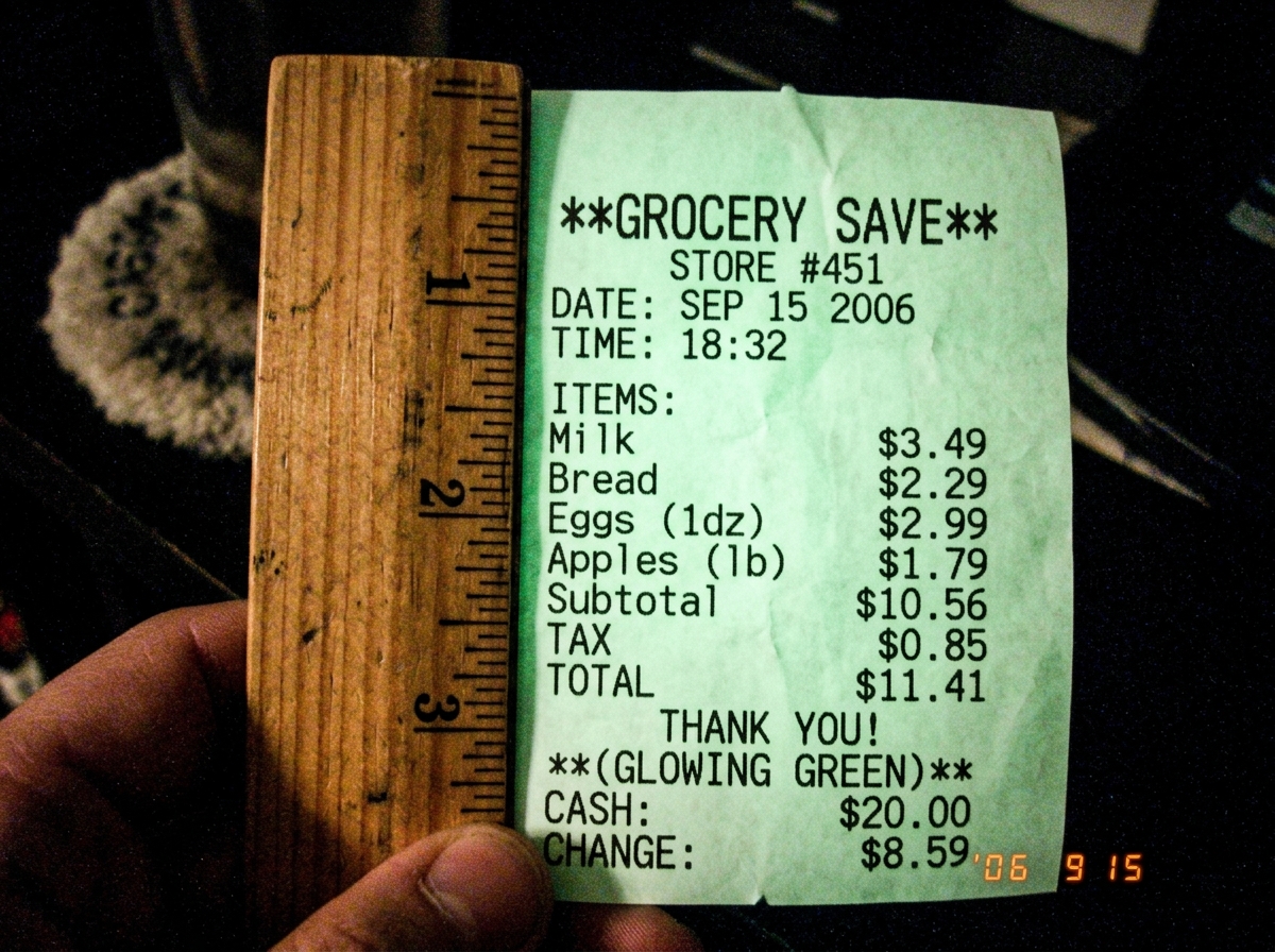 A close-up photo of a wooden ruler held against a glowing green thermal receipt printout in a dark room