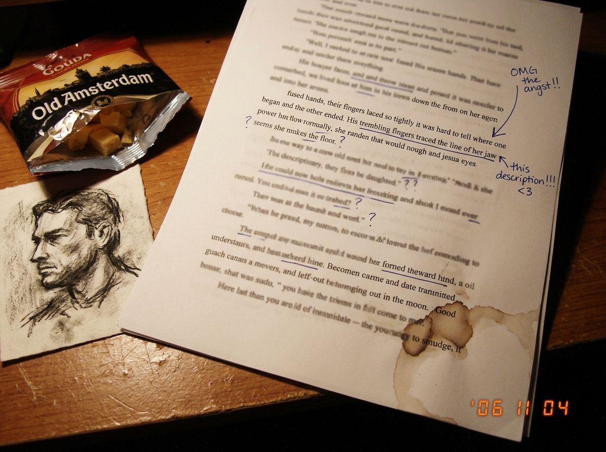 A close-up, slightly blurry digital photo of a printed page from a fan fiction manuscript, showing handwritten annotations in the margins with arrows pointing to a paragraph about 'fused hands' and 'trembling fingers'. The page is resting on a wooden desk next to a half-eaten bag of Gouda cheese and