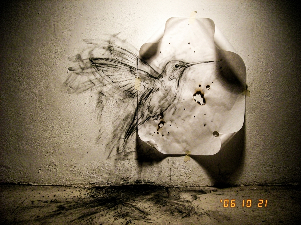 a close-up sketch of a wall in a dark studio, charcoal dust is visible on the floor, the paper used to trace lines is curled at the edges with small holes burnt through it, a faint outline of a humming hum is drawn in the charcoal that seems to vibrate around the edges