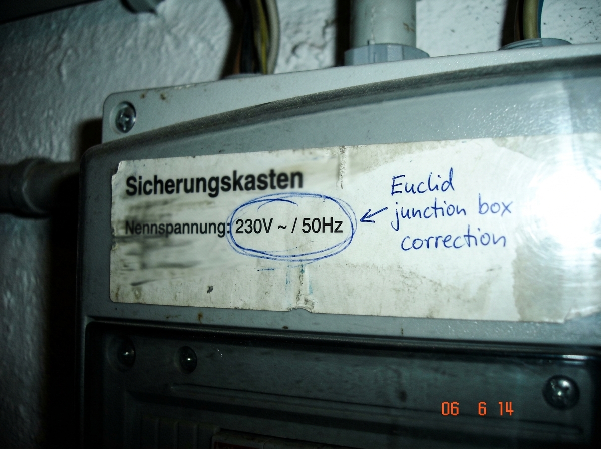A blurry photo of a German electrical panel label reading '50Hz / 230V ~' with a handwritten annotation in blue ink that says 'Euclid junction box correction' and a small red circle around the frequency specification. The photo is taken at a low angle with flash washout on the right side.