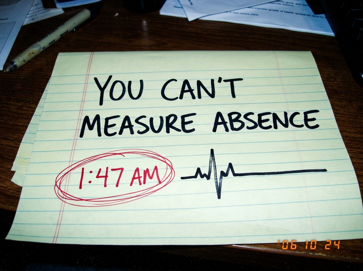a handwritten note on yellow legal pad paper that says 'YOU CAN'T MEASURE ABSENCE' in thick black marker, with '1:47 AM' circled in red underneath and a crude drawing of a flatline heart monitor graph