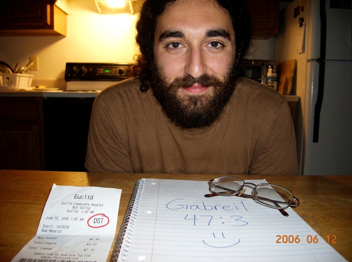 A crumpled Euclid bus receipt from June 12, 2006, timestamp showing 1:47 AM with a DST flag circled in red pen. Next to it on a wooden table, an open spiral notebook showing 'Gabreil 47:3' hand-written in blue ink with a small hand-drawn smiley face. A pair of reading glasses rests on the corner of 