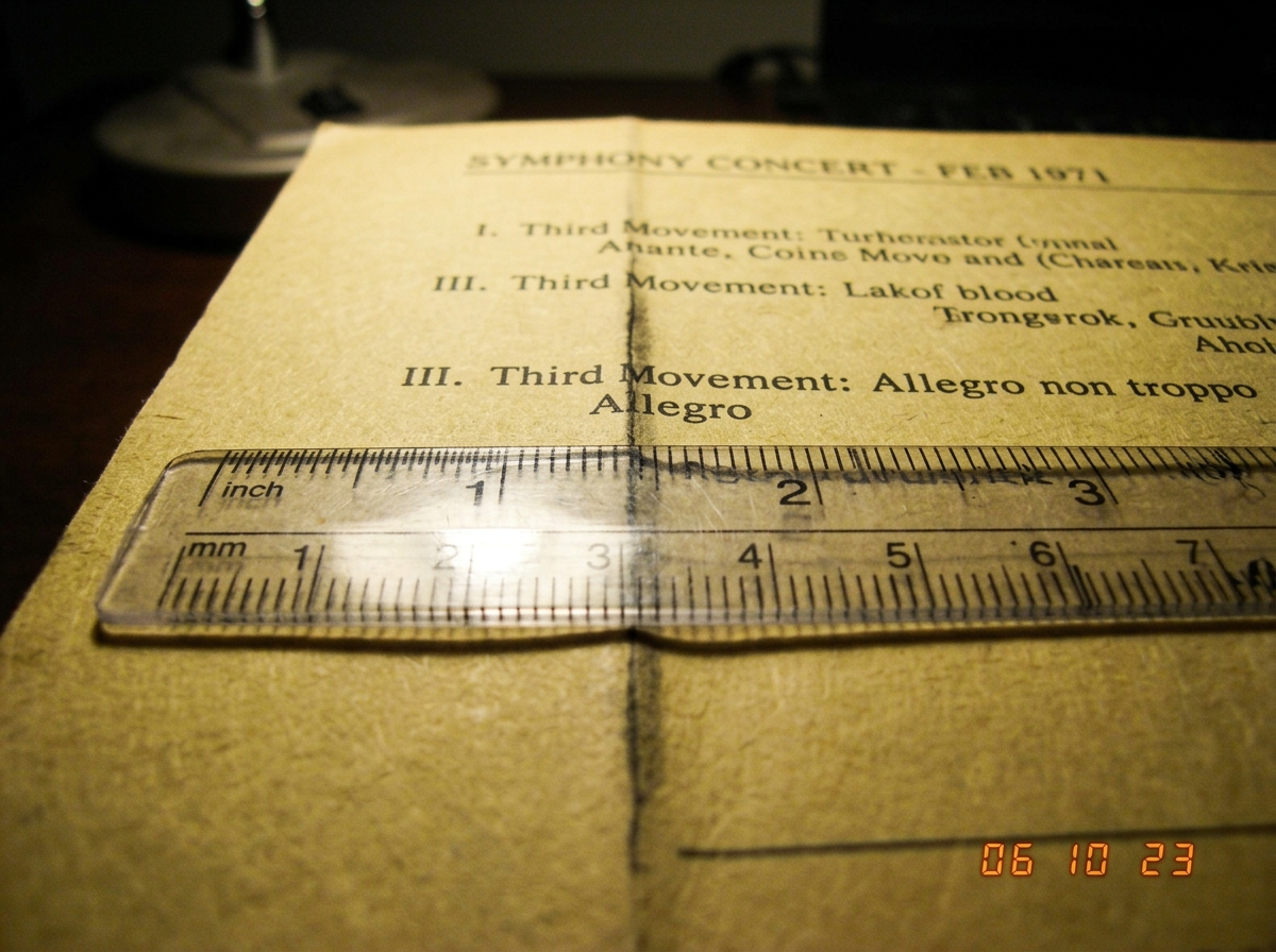 A close-up scan of a 1971 concert program insert, yellowed paper with a British Rail timetable texture. A visible printer's crease runs vertically at approximately 1.47 inches from the left edge. The crease intersects the word 'Allegro' in the third movement notation. A cheap plastic ruler is laid a