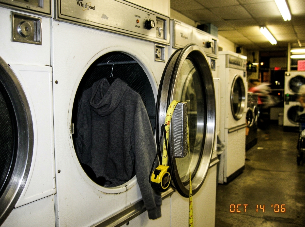 A blurry photo of a grey hoodie hanging in a laundromat dryer, with a measuring tape draped over the handle