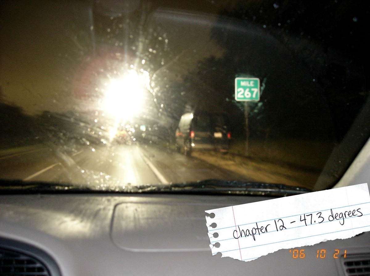 A blurry photo taken at night through a car windshield showing a highway mile marker 267. The camera flash reflects off the glass. A church van is barely visible parked on the shoulder ahead, its shape indistinct. In the bottom corner of the photo, a scrap of notebook paper has 'chapter 12 - 47.3 de