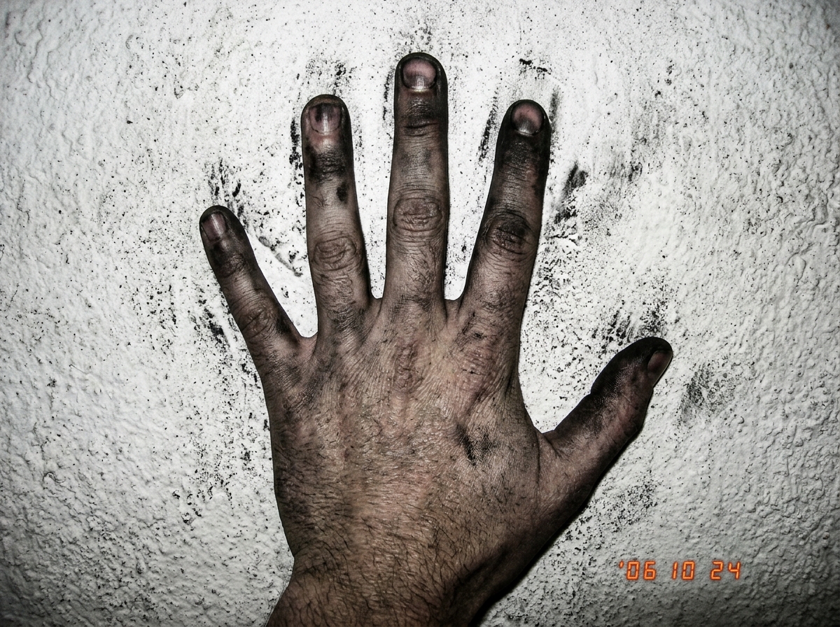 close-up of charcoal hand pressed flat against a rough plaster wall, dark smudges on fingertips, dust visible on the surface in high contrast