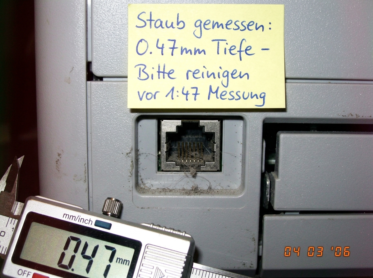 A close-up macro photograph of an RJ45 ethernet port on the back of a Brother HL-5040 laser printer. The port is partially filled with visible dust and lint. A yellow sticky note is attached to the printer壳体 above the port with handwritten text in blue ink: 'Staub gemessen: 0.47mm Tiefe - Bitte rein