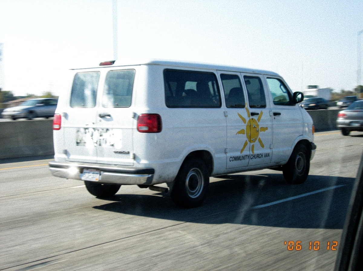 A blurry, low-resolution photo of a church van on I-80 with a sun symbol on the side door, taken from a moving car. The sun has eight rays but they are uneven and the paint is chipped. The license plate is partially obscured by glare.