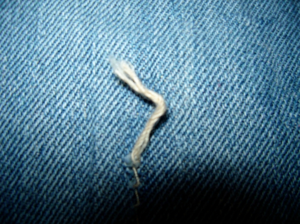 A heavily zoomed and cropped section of the 2003 Euclid parking lot cuff photo, showing the denim weave pattern in extreme close-up with a visible loose thread that appears to form a 47.3 degree angle against the weave grain. The image is slightly blurry but the angle of the thread is clearly unnatu