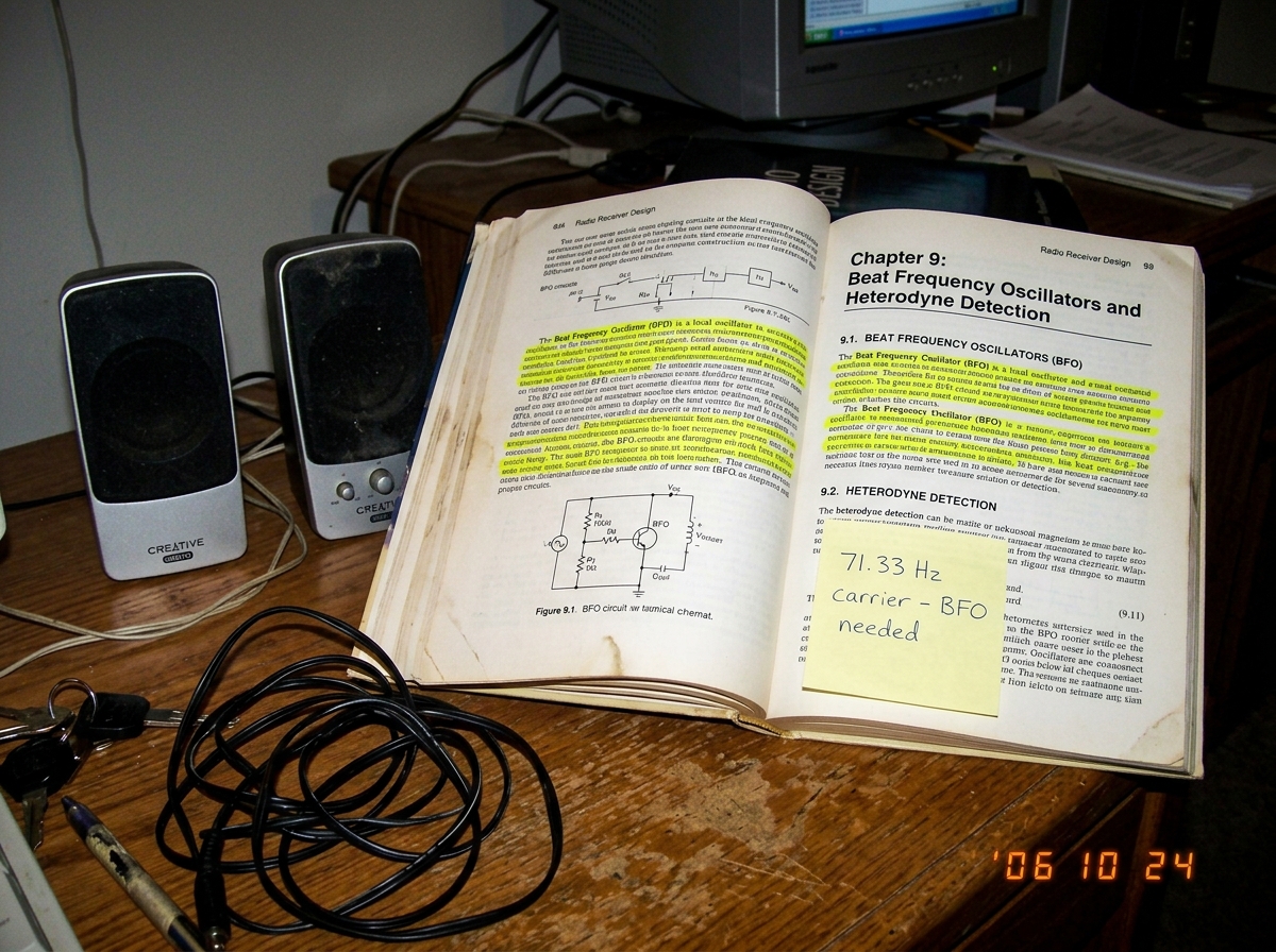 A close-up photo of a paperback book titled 'Radio Receiver Design' open to a page about beat frequency oscillators and heterodyne detection. The page has yellow highlighter marks on paragraphs about BFO circuits. A pair of small computer speakers sits to the left of the book, and a coiled headphone