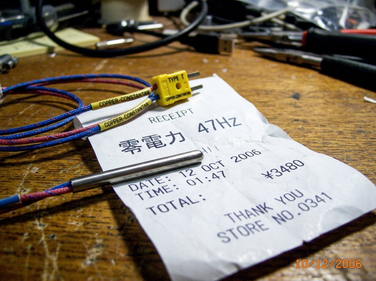 A close-up of a thermocouple probe (type T, labeled 'COPPER-CONSTANTAN') resting on a crumpled Euro-style thermal paper receipt with Japanese characters 零電力 47Hz faintly visible, timestamp 01:47.