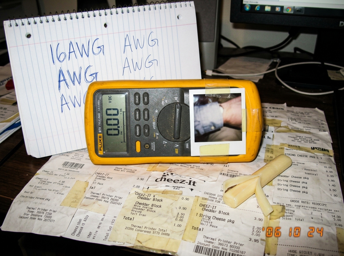 A photo of a Fluke 87V multimeter sitting on top of a crumpled cheese receipt shrine collage, with a tiny cuff photo taped to the side and a spiral notebook page showing '16AWG AWG AWG' written in ballpoint. A small piece of string cheese sits next to the meter.