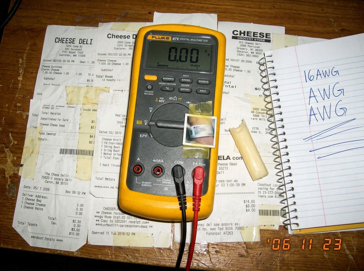 A Fluke 87V multimeter sitting on top of a crumpled cheese receipt shrine collage, with a tiny cuff photo taped to the side and a spiral notebook page showing '16AWG AWG AWG' written in ballpoint. A small piece of string cheese sits next to the meter.