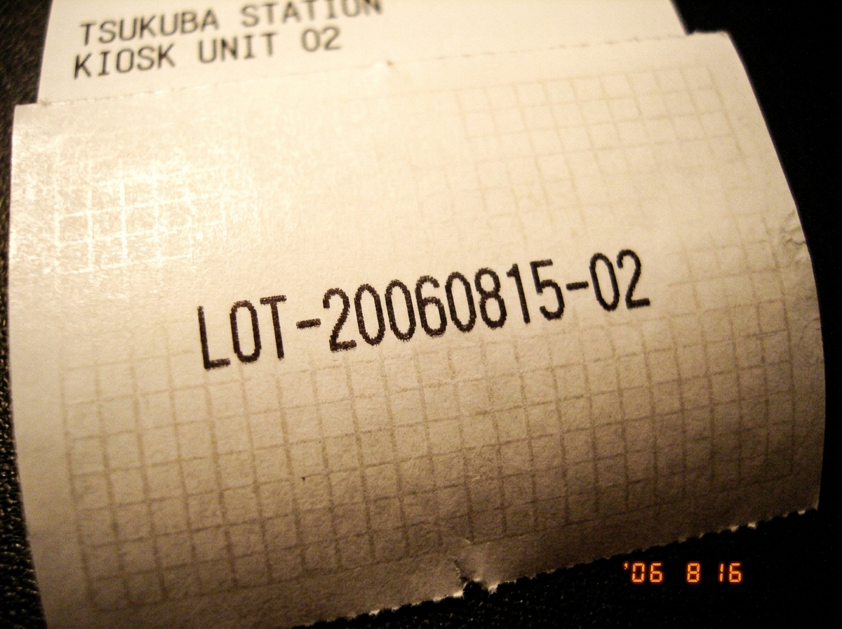 A close-up of the back of a thermal paper receipt from Tsukuba Station kiosk Unit 02 showing a printed core lot number 'LOT-20060815-02' and a faint grid pattern matching the spectral artifact.
