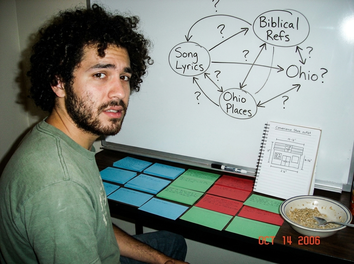 A photograph taken at a desk cluttered with index cards in three colors (blue, green, red) organized in rows. In the foreground, a whiteboard propped against a bookshelf shows a detailed diagram of Gabriel Chantayan's song lyrics connected to biblical references and Ohio place names, with arrows and