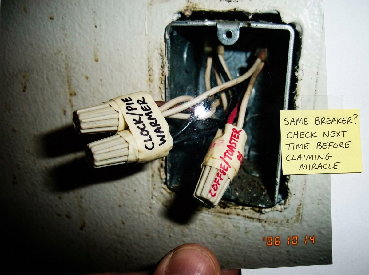 A hastily photographed diner wall outlet with the cover plate removed, showing two sets of wire nuts - one labeled 'CLOCK/PIE WARMER' in black marker on electrical tape, the other labeled 'COFFEE/TOASTER' in red marker. The photo is blurry and taken at a bad angle, with a thumbnail partly in frame. 