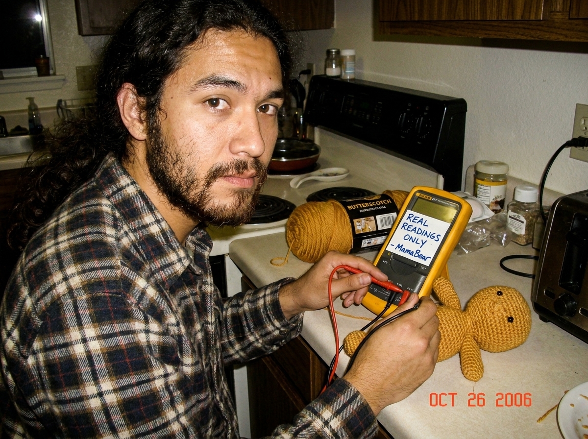 A photo of a Fluke 87V multimeter sitting on a kitchen counter next to a butterscotch-colored yarn skein and a half-finished crocheted Gabriel amigurumi doll, with a handwritten note taped to the meter that says 'REAL READINGS ONLY - MamaBear' in blue Sharpie