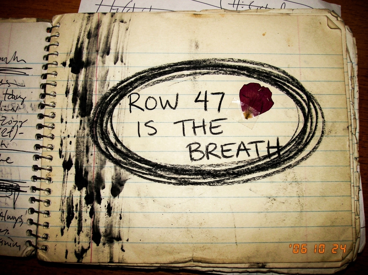 A page from a handwritten notebook with the words 'ROW 47 IS THE BREATH' circled three times in charcoal, with a pressed flower petal next to the number 47 and smudged ink running down the margin like rain