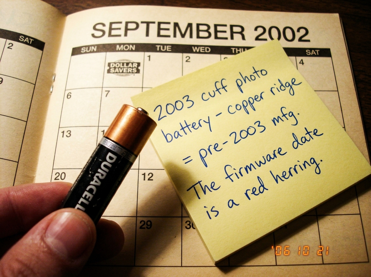A close-up scan of a Duracell AA battery held against a 2002 calendar page. The battery has the copper-top ridge design with the old-style DURACELL logo font, and the calendar is open to September 2002 from a dollar store promotional giveaway. A sticky note with handwritten ballpoint pen reads: '200