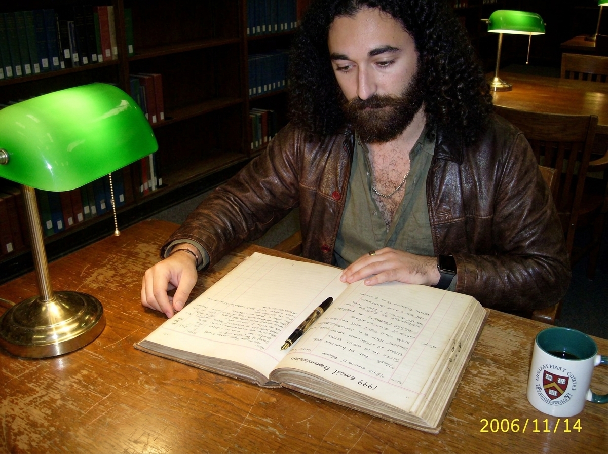 A worn wooden library reading desk with a green banker's lamp. An open archival ledger with careful handwritten notes in black ink, referencing Gabriel Chantayan's 1999 email transmission. A fountain pen rests on the page. The edges of the paper are yellowed. A coffee mug with the library crest is v