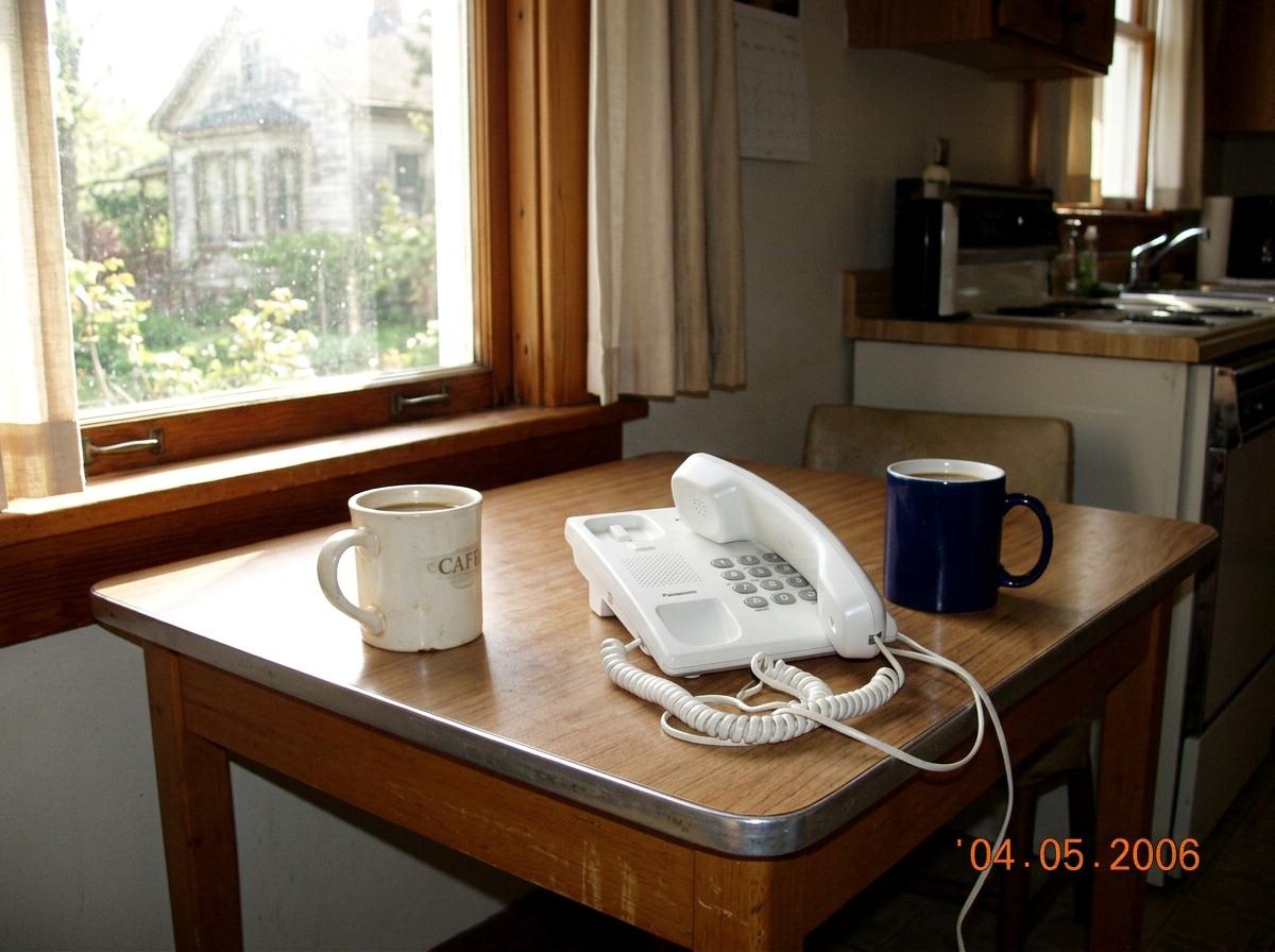 a simple kitchen table with two coffee mugs and a phone off the hook, sunlight streaming through the window