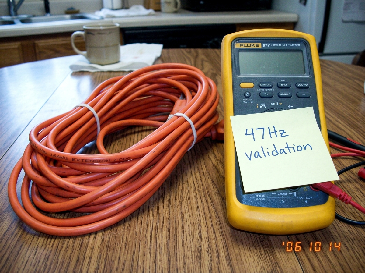 A 16awg extension cord coiled on a kitchen table next to a Fluke 87V multimeter with a sticky note that says 47Hz validation