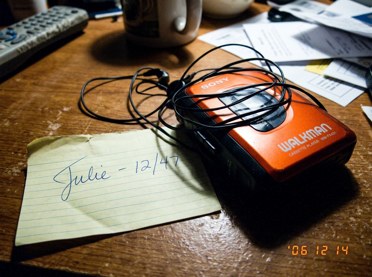 a vintage Sony Walkman with tangled headphones sitting next to a handwritten note that says 'Julie - 12/47' in messy cursive