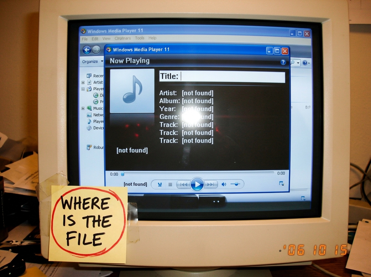 A crudely edited screenshot of a Windows Media Player window showing 'Now Playing' with the title field blank and metadata fields all reading 'not found'. A handwritten sticky note on the monitor reads 'WHERE IS THE FILE' in black marker with a red circle around it.