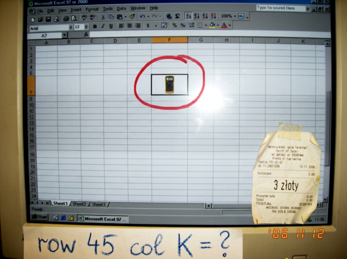 Screenshot of an empty spreadsheet cell with a red sharpie circle around a tiny Fluke 87V icon, crayon text at bottom saying 'row 45 col K = ?', and a cheese receipt reading '3 zloty' in the corner