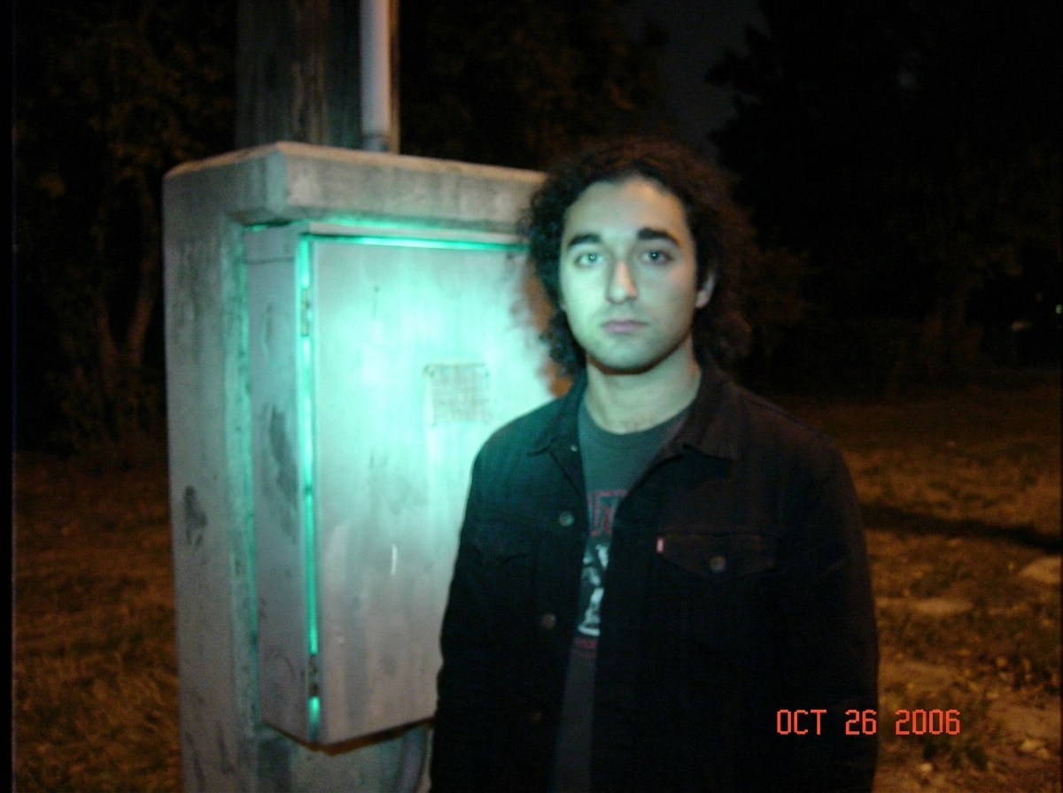a blurry, grainy photo of a concrete electrical junction box at night with a strange greenish-blue glow emanating from the seams, looking like a bad screenshot from a VHS tape
