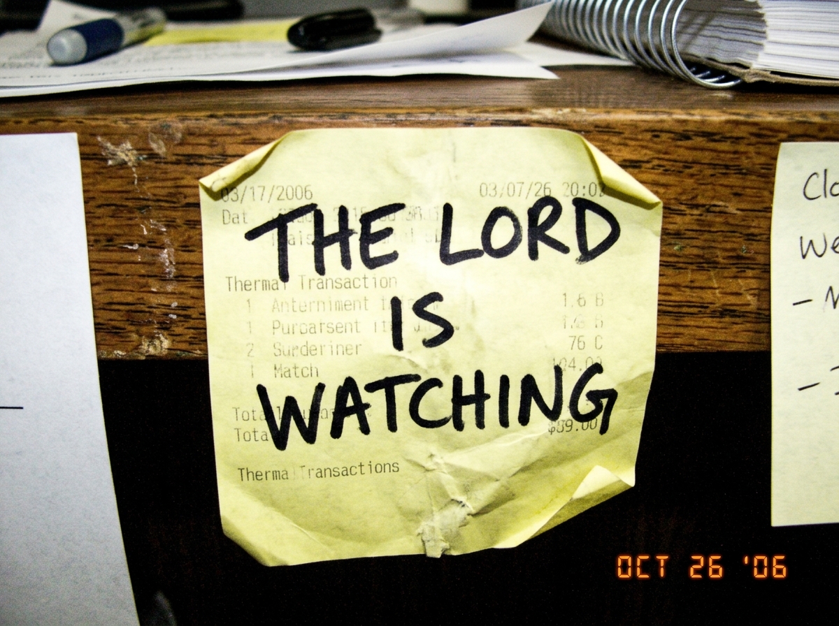 a crumpled, thermal-printed receipt on a sticky note with the text 'THE LORD IS WATCHING' handwritten over the printed area in sharpie