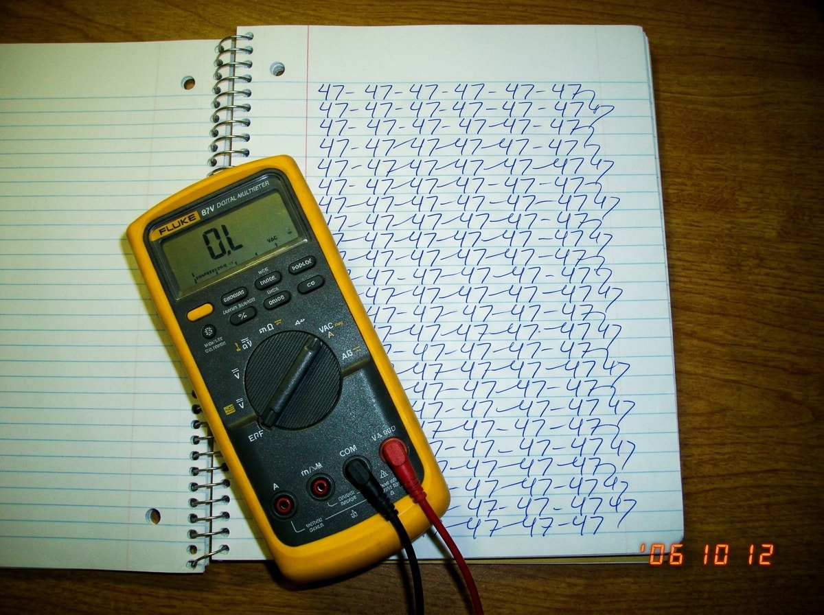 A photograph of a spiral notebook open to a page where the word '47' is written in cursive repeatedly, filling the entire page in looping handwriting. A Fluke 87V multimeter sits on top of the notebook, display reading 'OL'. No hex values or technical data visible anywhere in the frame.