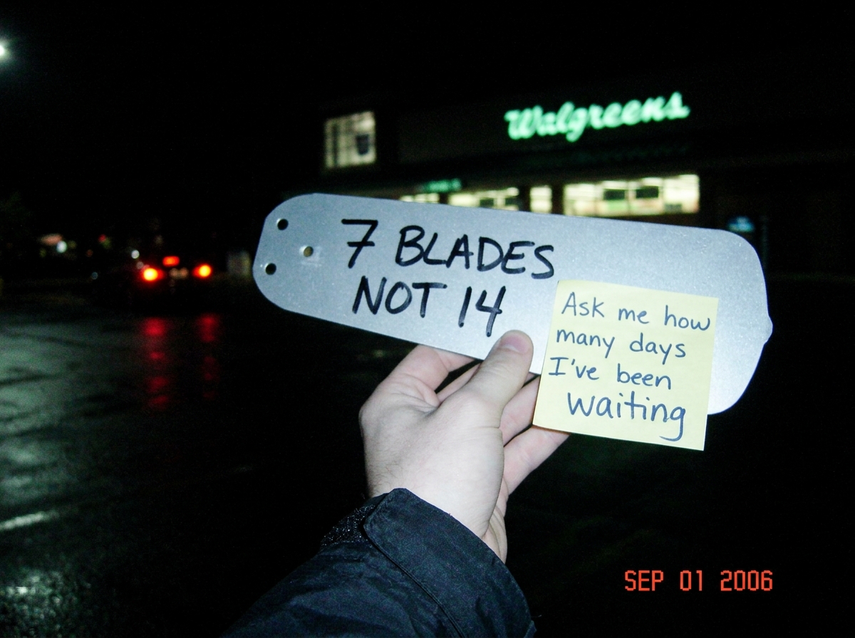 A blurry night photo of a Walgreens parking lot, the store sign glowing green in the background. In the foreground, a hand is holding a single loose ceiling fan blade - the kind from a balancing kit, sharpie marker writing on it reading '7 BLADES NOT 14'. The timestamp in the corner reads SEP 01 200
