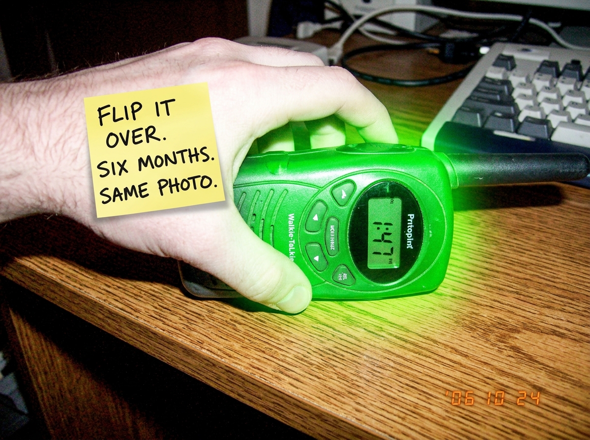 A crudely edited photo showing the same green-glowing walkie talkie GuardiaoDaNoite always posts, but someone has photoshopped a hand reaching into the frame to flip it over. The hand has a sticky note on it reading 'FLIP IT OVER. SIX MONTHS. SAME PHOTO.' drawn in black marker. The walkie's display 
