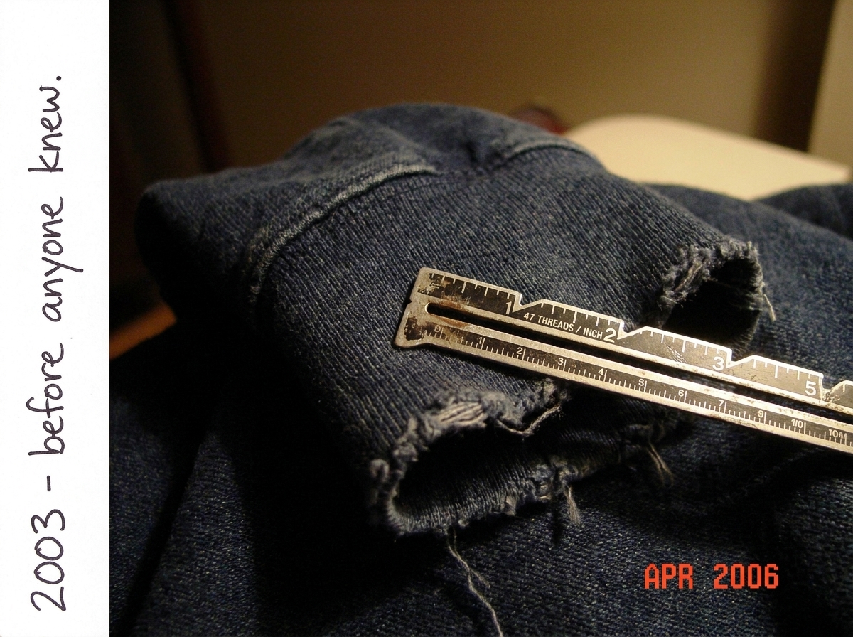 Close-up photo of a dark denim hoodie cuff, frayed at the edge. A sewing gauge with threads per inch scale lies across the fabric showing 47 threads aligned with the gauge marks. Handwritten note in the margin says '2003 - before anyone knew.' The photo is dated April 2006 in the corner.