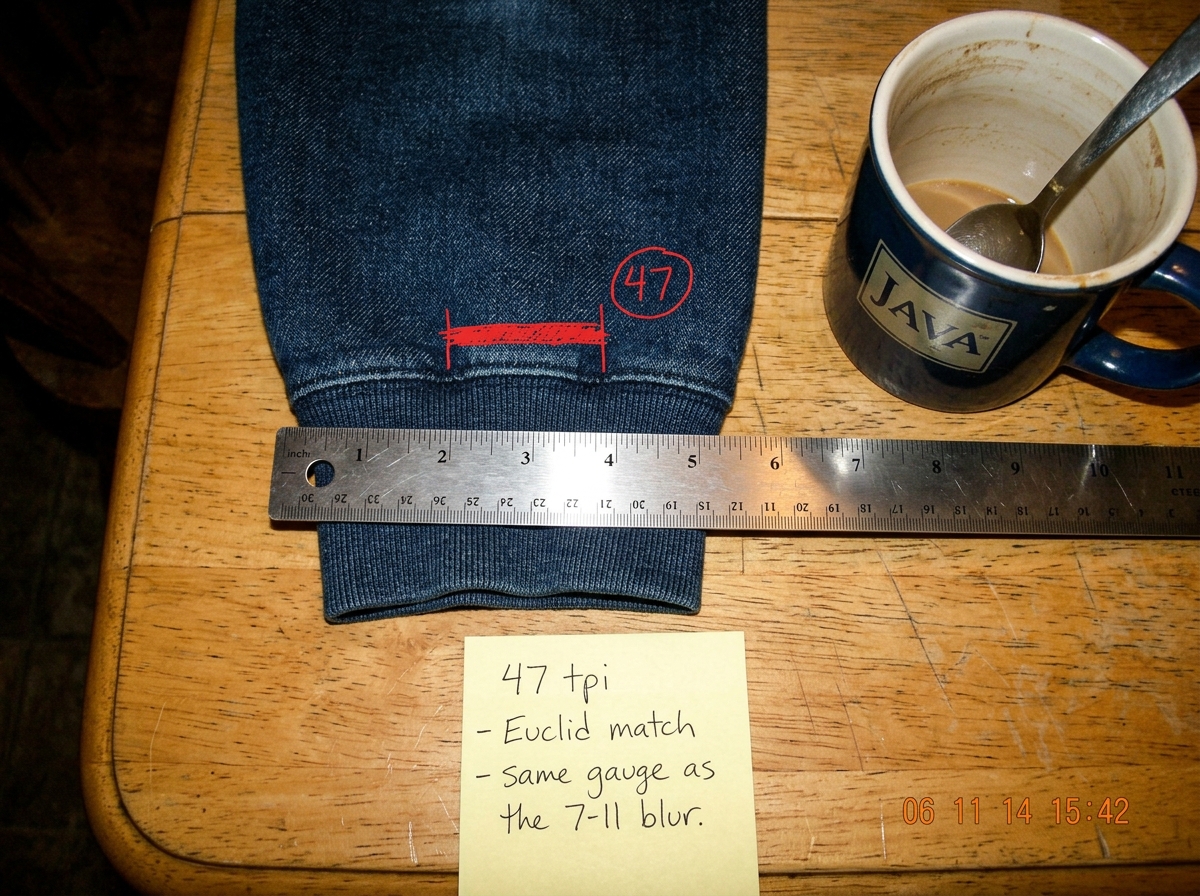 A close-up scan of a denim hoodie cuff laid flat against a ruler. The weave is clearly visible - 47 threads counted per inch marked with a red pen stroke. A sticky note at the bottom reads '47 tpi - Euclid match - same gauge as the 7-11 blur.' The photo is taken on a kitchen table next to a coffee m