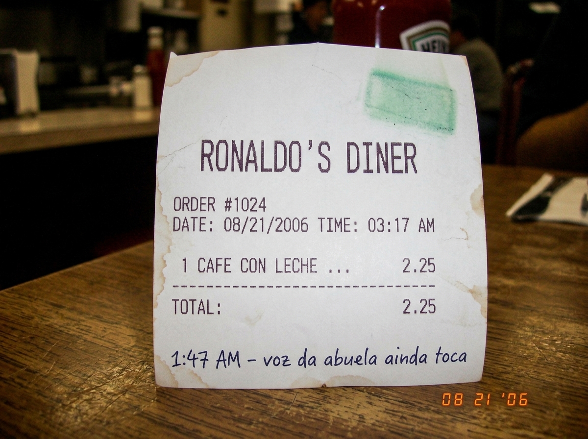 Thermal paper receipt from Ronaldo's Diner showing 'cafe con leche' purchased at 3:17 AM, faint green smudge in corner where walkie talkie glow pressed against counter, coffee-stained edges curled, handwritten '1:47 AM - abuela voice still plays' in Portuguese at bottom