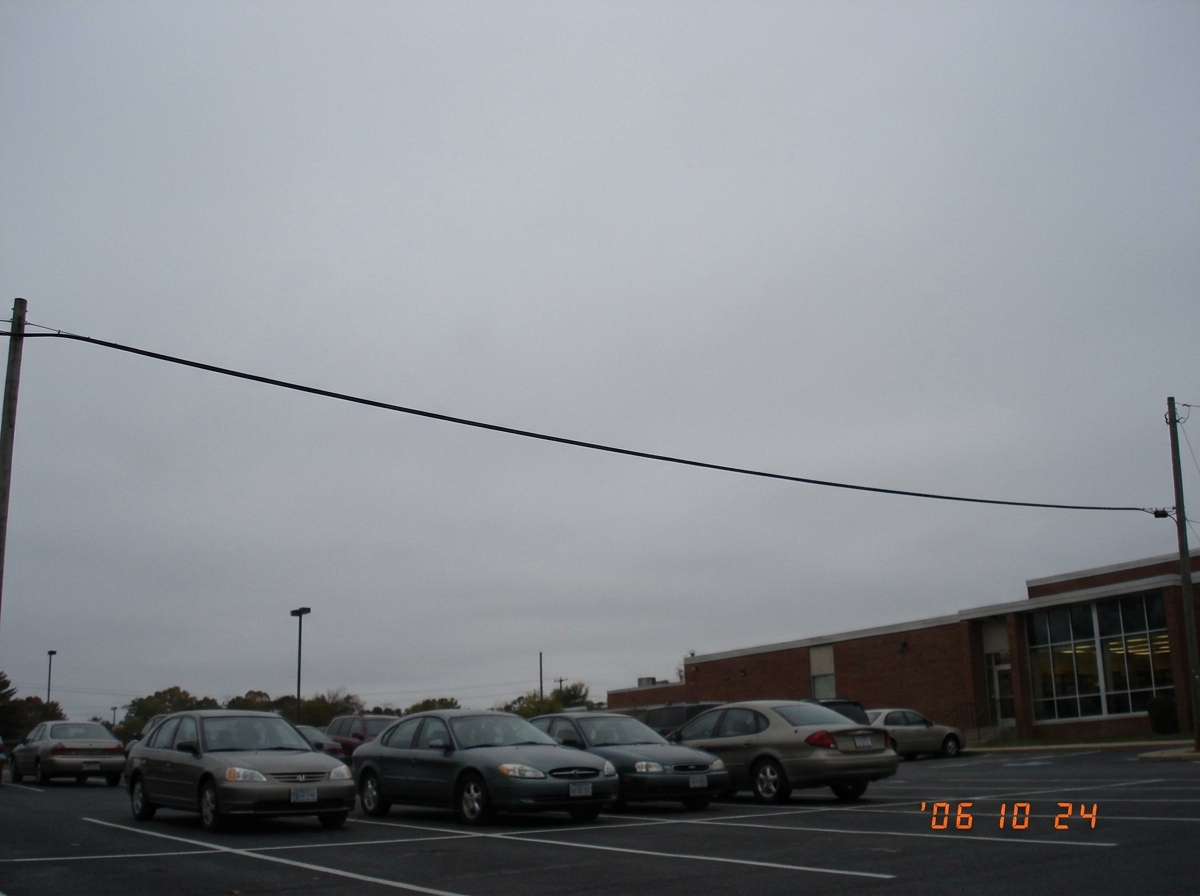 A photograph of an overcast sky taken from a library parking lot. No clouds in any discernible pattern matching any claimed thermal interval. Just grey sky and a telephone wire crossing the upper left corner. Evidence of what proper documentation looks like: nothing claimed, everything recorded.