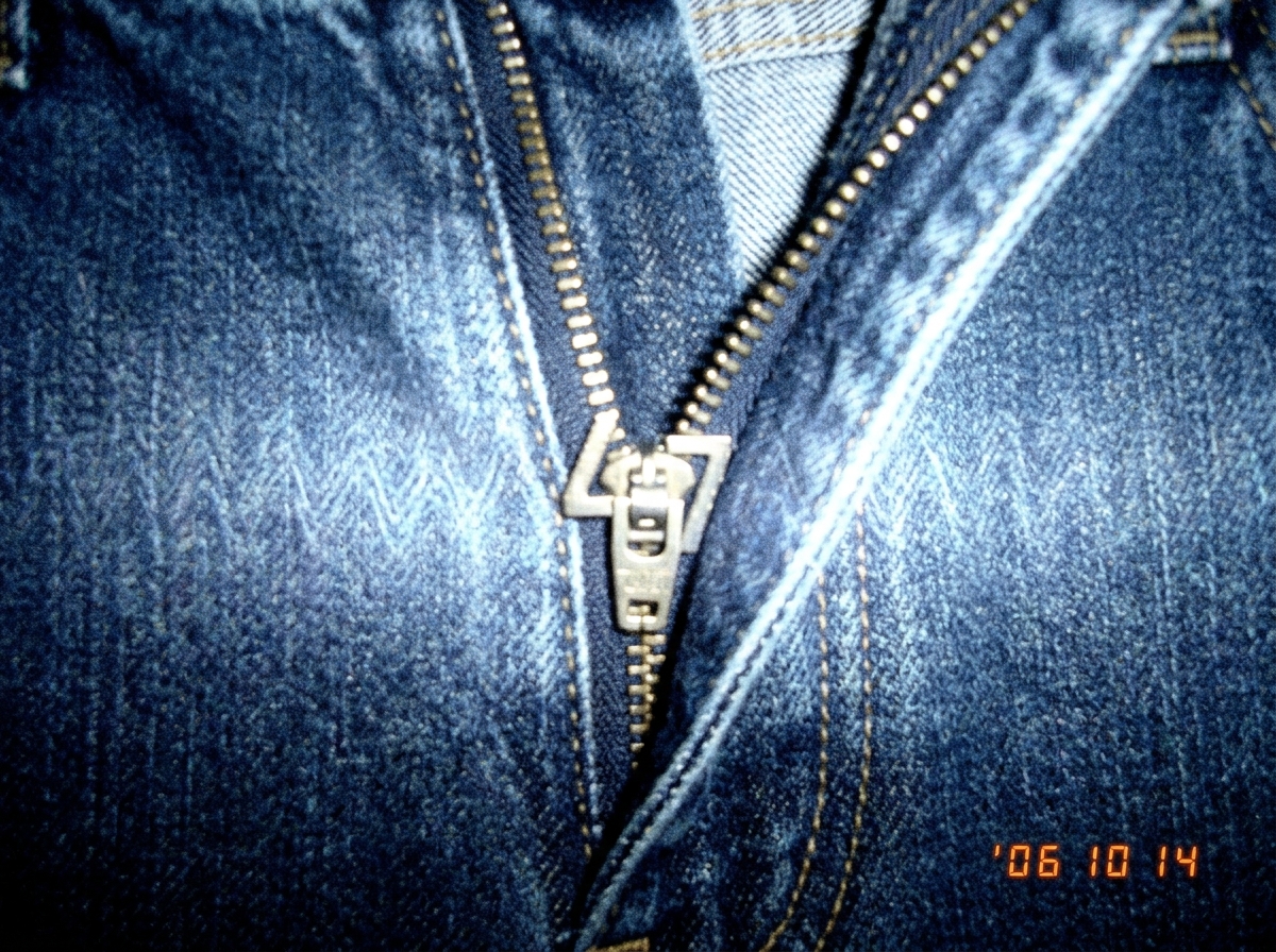 A close-up of a pair of jeans with the zipper pulled halfway down, the teeth forming a perfect '47' shape. The denim weave is subtly glowing with a faint 47Hz sine wave pattern visible only in the right light. The photo is slightly overexposed to emphasize the glow.