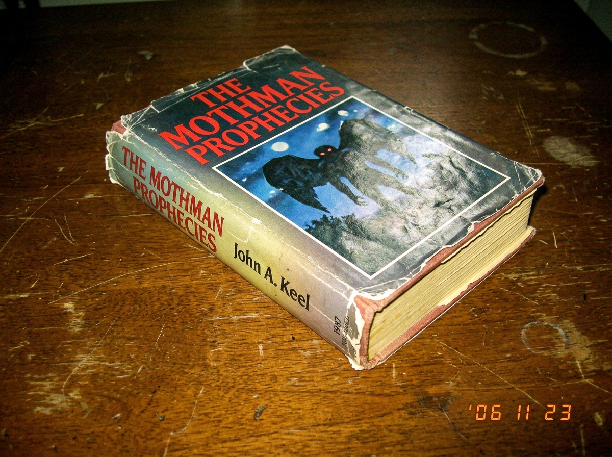 A worn 1987 hardcover of The Mothman Prophecies, pages slightly yellowed, sitting on a wooden table