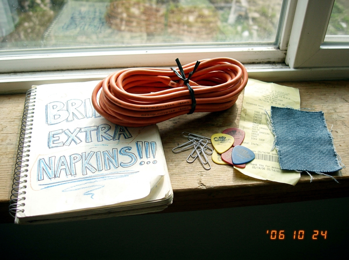 A photo of BestBuddyStar's 16AWG extension cord coiled next to her notebook that says 'bring extra napkins!!!' in bubble letters, with a small shrine of paperclips, guitar picks, cheese receipt, and denim swatch arranged on a windowsill with morning light.