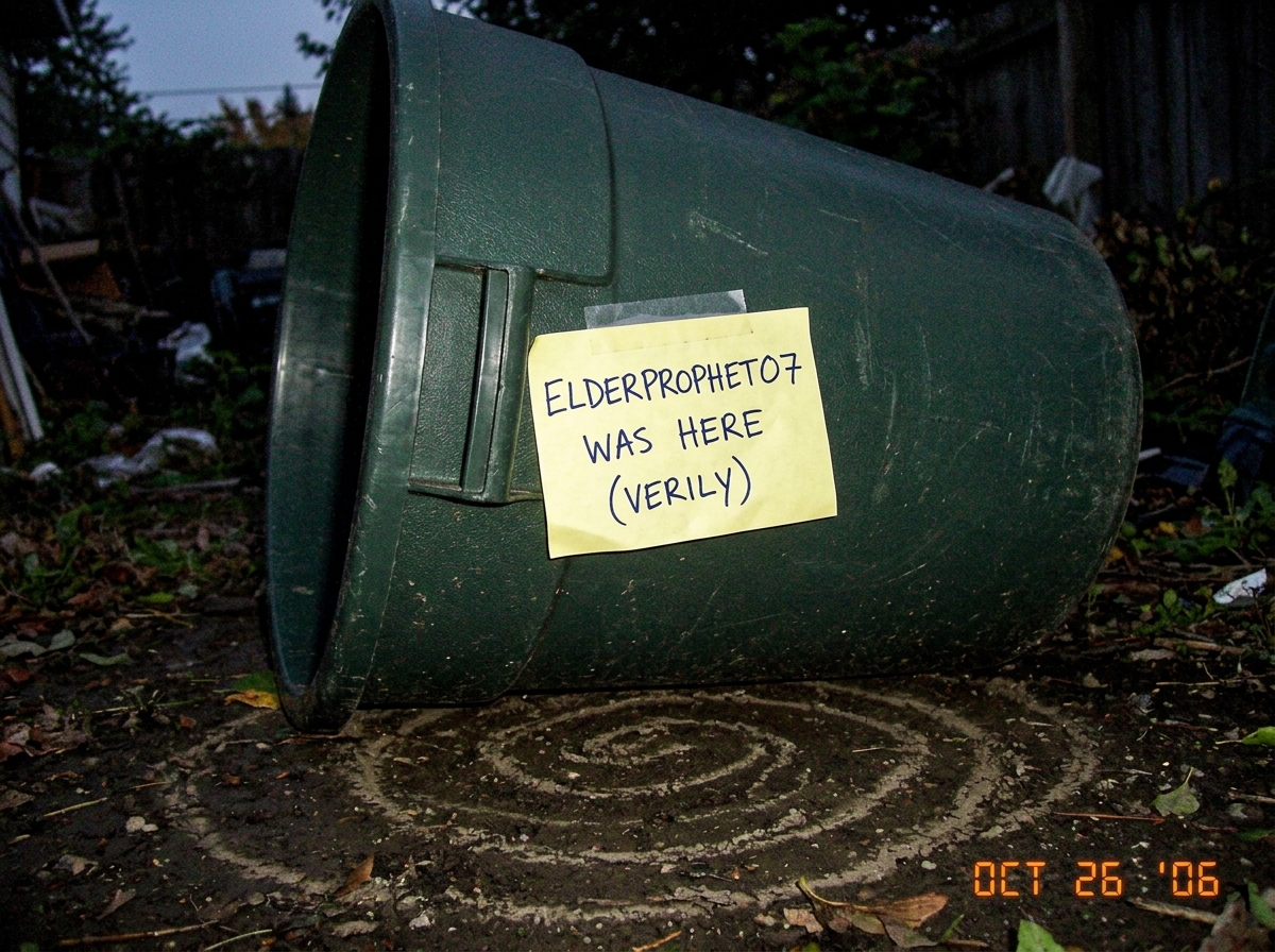 A grainy photo of a garbage can tipped over in a yard at dusk, with a handwritten sticky note taped to the can reading 'ELDERPROPHET07 WAS HERE (VERILY)' in all caps. A spiral pattern is visible in the dirt underneath. The photo is taken from a low angle making the can look larger than life.